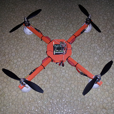 An orange quadcopter made of salvaged model airplane parts and cheap pine